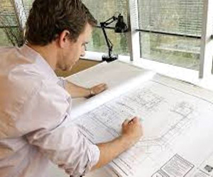 man sitting at a desk, looking at building plans